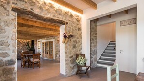 A rustic interior with stone walls, wooden beams, a staircase, and a dining area with chairs and a table. - Gorgeous home in Canyamel with private swimming pool, can be inside or outside (Canyamel)