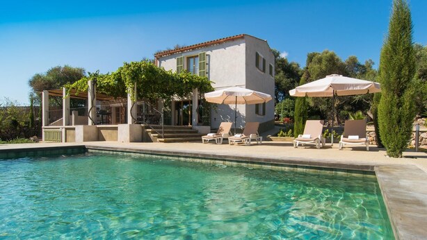 A clear pool with lounge chairs and umbrellas, a covered patio, and a building with a tiled roof. - Gorgeous home in Canyamel with private swimming pool, can be inside or outside (Canyamel)