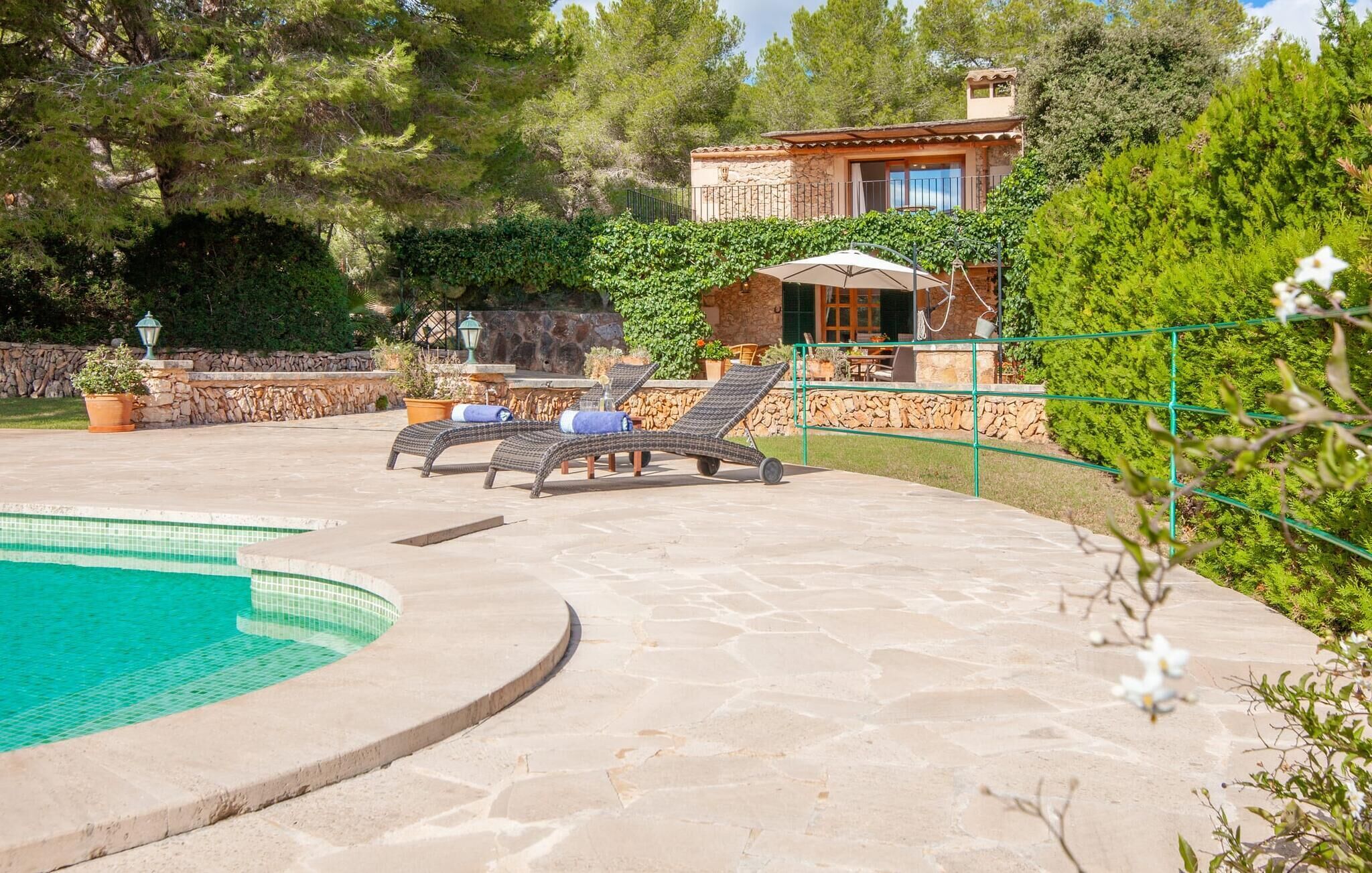 Zona de piscina amb gandules, un pati de pedra i un edifici de pedra amb un balcó.