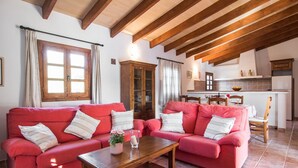 Una sala de estar acogedora con sofás rojos y una mesa de centro de madera, una cocina con armarios blancos, y un comedor con sillas de madera.