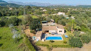 Una villa con piscina, rodeada de exuberante vegetación y montañas al fondo.