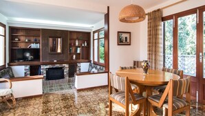 A living room with a fireplace, a dining area with a wooden table and chairs, and a large window with curtains. - Beach front home in Canyamel (Canyamel)
