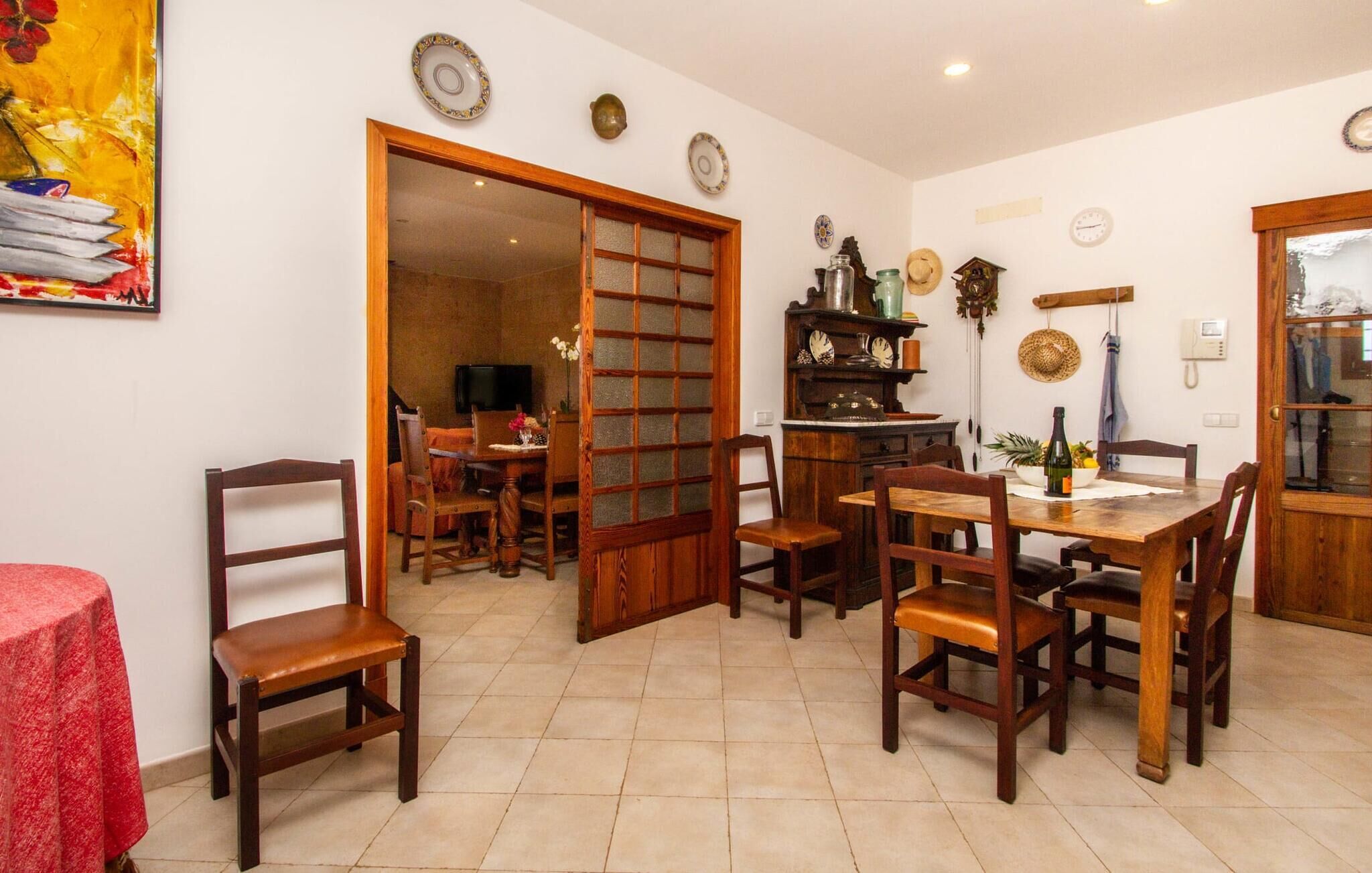 Uma área de refeições com móveis de madeira, piso ladrilhado e toalha de mesa vermelha.