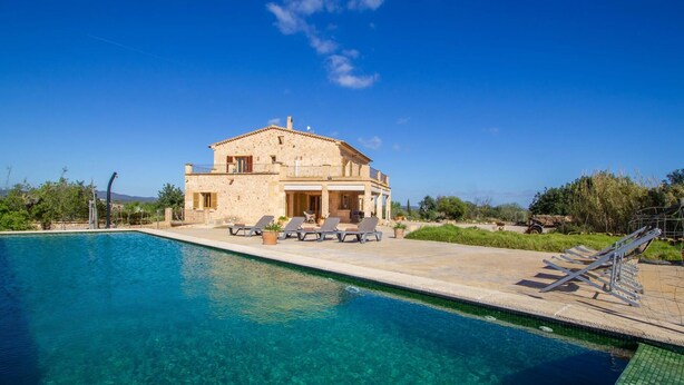 Ein zweistöckiges Steinhaus mit Swimmingpool und Sitzgelegenheit im Freien.