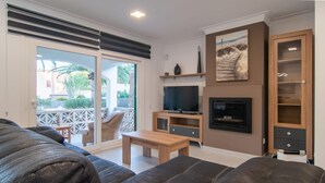 Un salon comprenant un canapé, un téléviseur, une cheminée et un balcon aménagé avec du mobilier d’extérieur.