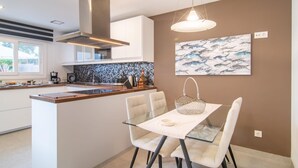 Une cuisine moderne dotée d’un îlot central, de meubles blancs, d’un pare-feu en carreaux noirs et d’un coin repas avec une table en verre et des chaises blanches.