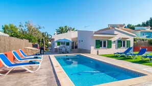 Une piscine avec des chaises longues, un espace patio et un bâtiment aux volets verts.