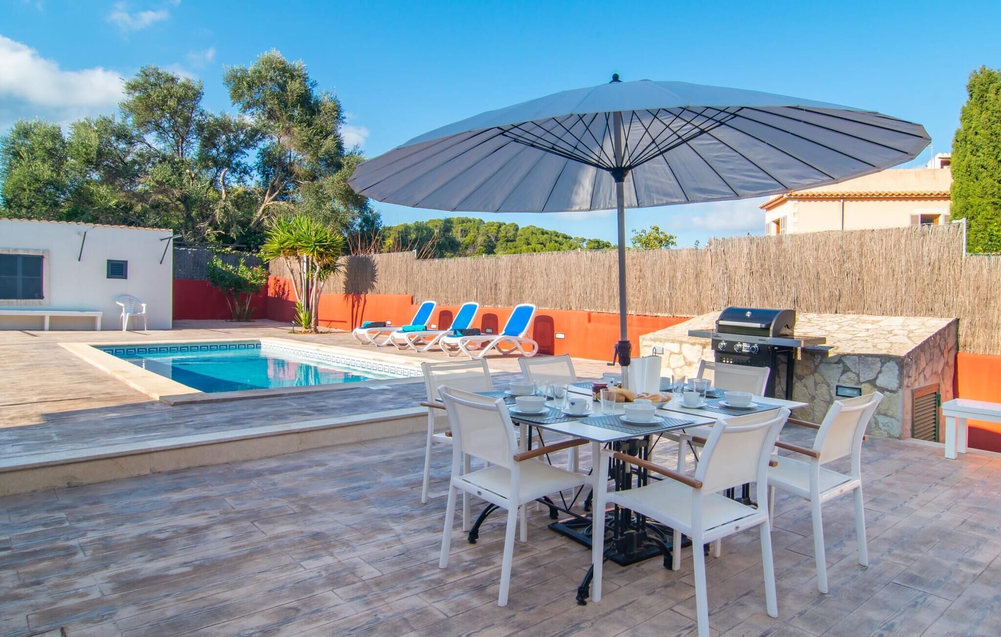 A poolside area with a table set for dining, lounge chairs, and a grill.