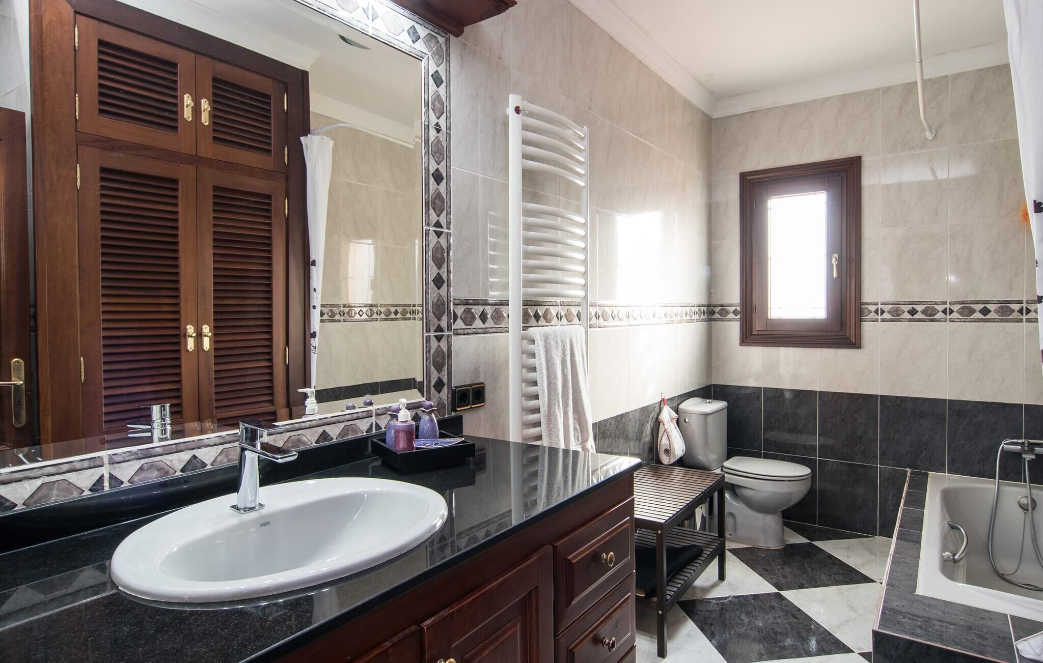 A bathroom with a large mirror, wooden cabinets, a sink, a toilet, and a shower area.