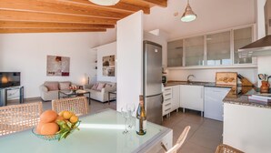 Una cucina moderna con mobili bianchi, lavastoviglie integrata e zona pranzo con tavolo in vetro e sedie in vimini.