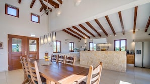 Un vaste espace à manger avec une table et des chaises en bois, une cuisine dotée de plans de travail en pierre et un plafond haut avec des poutres apparentes.