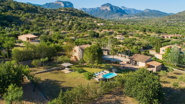 Een landelijk gebied met huizen, een zwembad en bergen op de achtergrond.