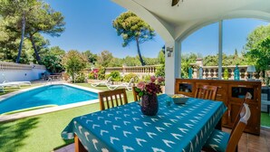 Un'area esterna riparata con piscina, un tavolo e sedie, e vista sul giardino e gli alberi circostanti.