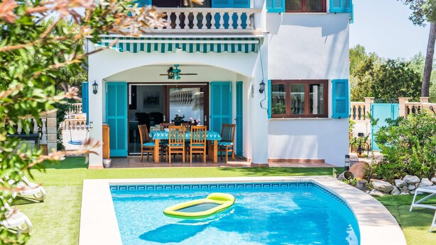 Una casa a due piani con piscina, zona pranzo con mobili da esterno e giardino.