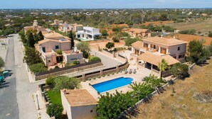 A residential area with a large swimming pool surrounded by houses, a clear sky, and a distant view of a town. - Lovely home in Cala Santanyi (Cala Santanyi)