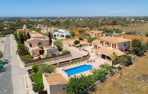A residential area with a large swimming pool surrounded by houses, a clear sky, and a distant view of a town. - Lovely home in Cala Santanyi (Cala Santanyi)