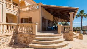 A multi-level building with a covered patio area, stone steps, and a palm tree in the background. - Lovely home in Cala Santanyi (Cala Santanyi)
