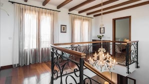A spacious room with wooden beams on the ceiling, a chandelier, and a wooden staircase with wrought iron railings. - Lovely home in Cala Santanyi (Cala Santanyi)