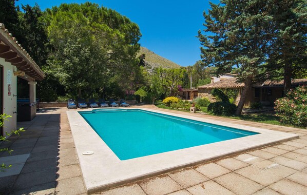 A rectangular swimming pool with a tiled deck, surrounded by lush greenery and a mountain in the background. - Beautiful home in Pollenca with private swimming pool, can be inside or outside (Pollenca)