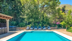 Piscina retangular com um deck revestido, rodeada por espreguiçadeiras e uma pérgula.