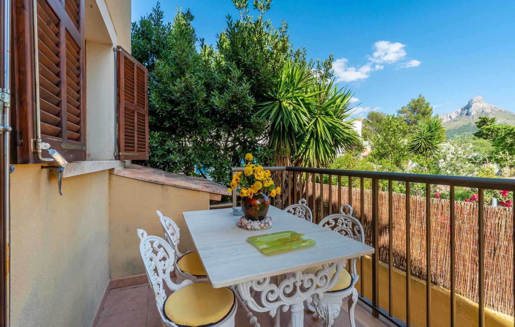 A balcony with a table, chairs, and a vase of flowers.