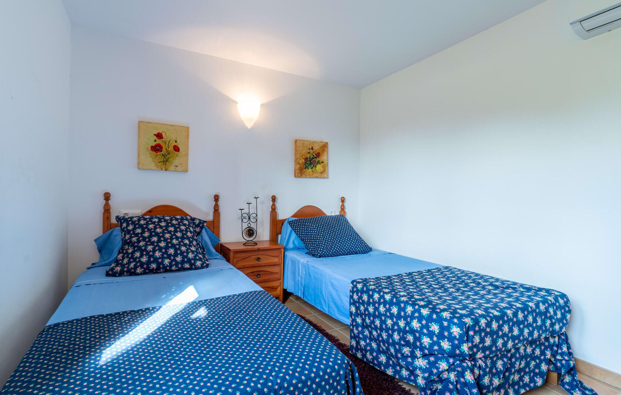 Una camera da letto con due letti, ciascuno con una coperta a motivi floreali, una testiera in legno e un comodino con un portacandele.