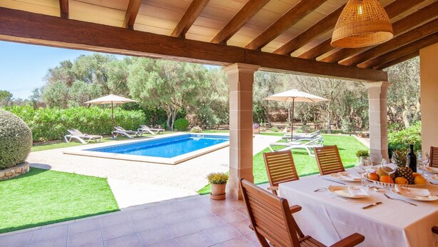 Un espacio al aire libre techado con piscina, sillas de descanso y una mesa dispuesta para comer.