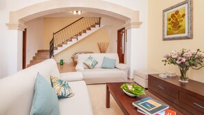 Una sala de estar con un sofá blanco, una mesa de centro de madera y una escalera que conduce a un piso superior.