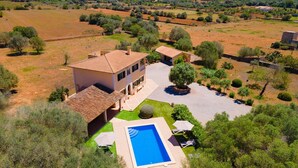 Una casa de dos plantas con piscina, rodeada de olivos y campos abiertos.