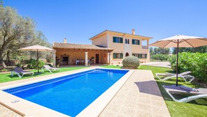 Una casa de dos pisos con piscina, mobiliario exterior y un jardín cuidado.