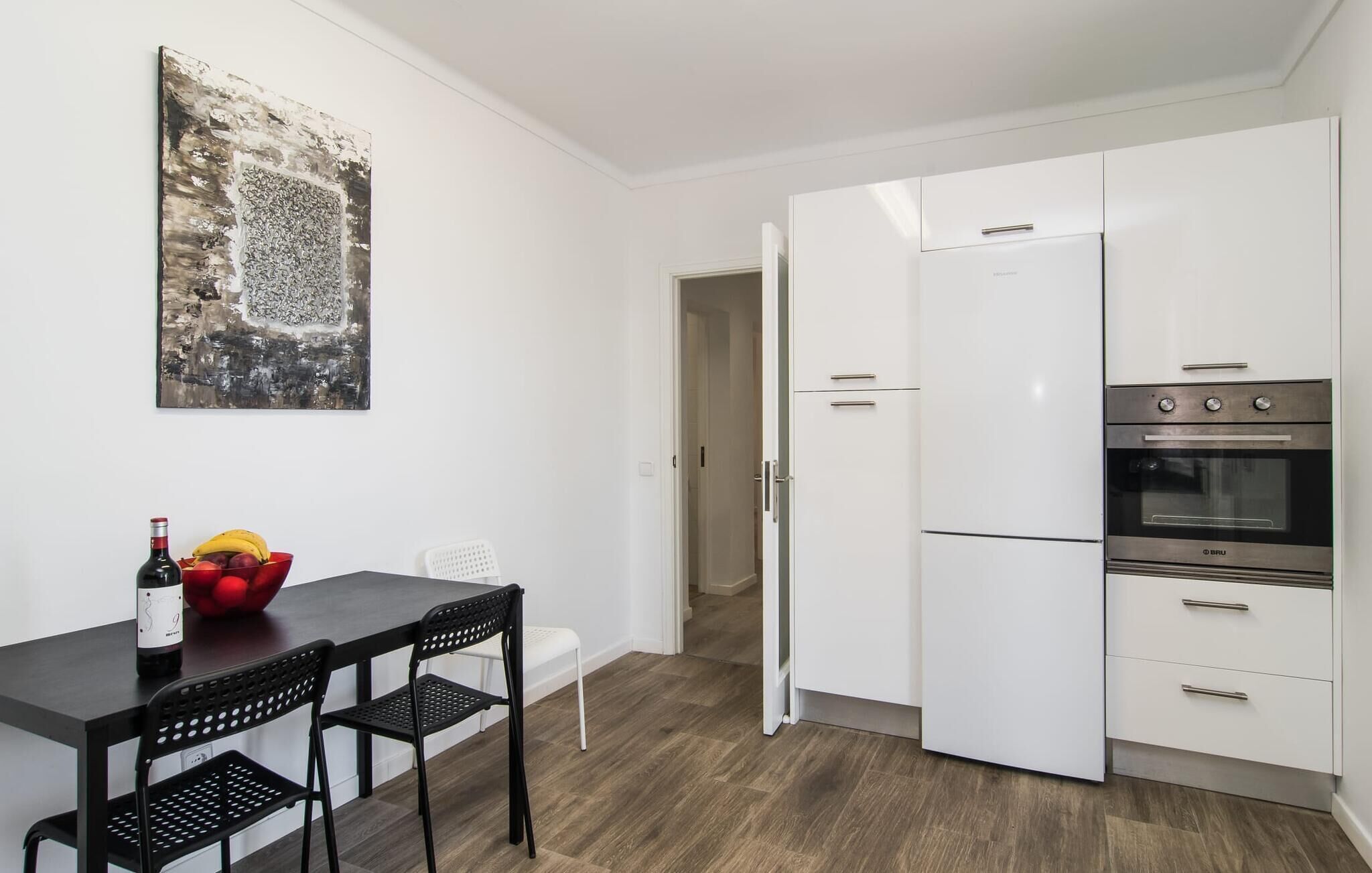 A compact kitchen with white cabinets, a built-in oven, and a dining area with a table and chairs.