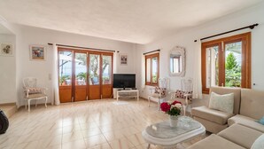 Un salón espacioso con un televisor grande, asientos cómodos y vistas al exterior.