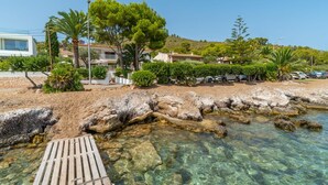 Una zona costera con aguas cristalinas, un muelle de madera y edificios residenciales al fondo.