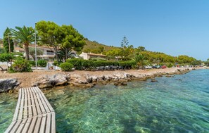 A coastal property with a wooden pier leading into clear waters, surrounded by lush greenery and parked cars. - Awesome home in Alcudia with WiFi (Alcudia)