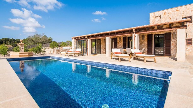 A swimming pool with lounge chairs and a stone building with large windows.