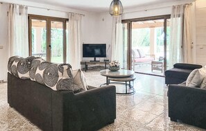 A living room with a sofa, a TV, a round table, and a view of the outdoors through large windows. - Stunning home in Cala dOr with private swimming pool, can be inside or outside (Cala dOr)