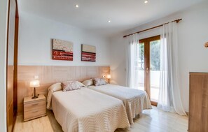 Een slaapkamer met twee bedden, een nachtkastje, een lamp en een houten garderobe.