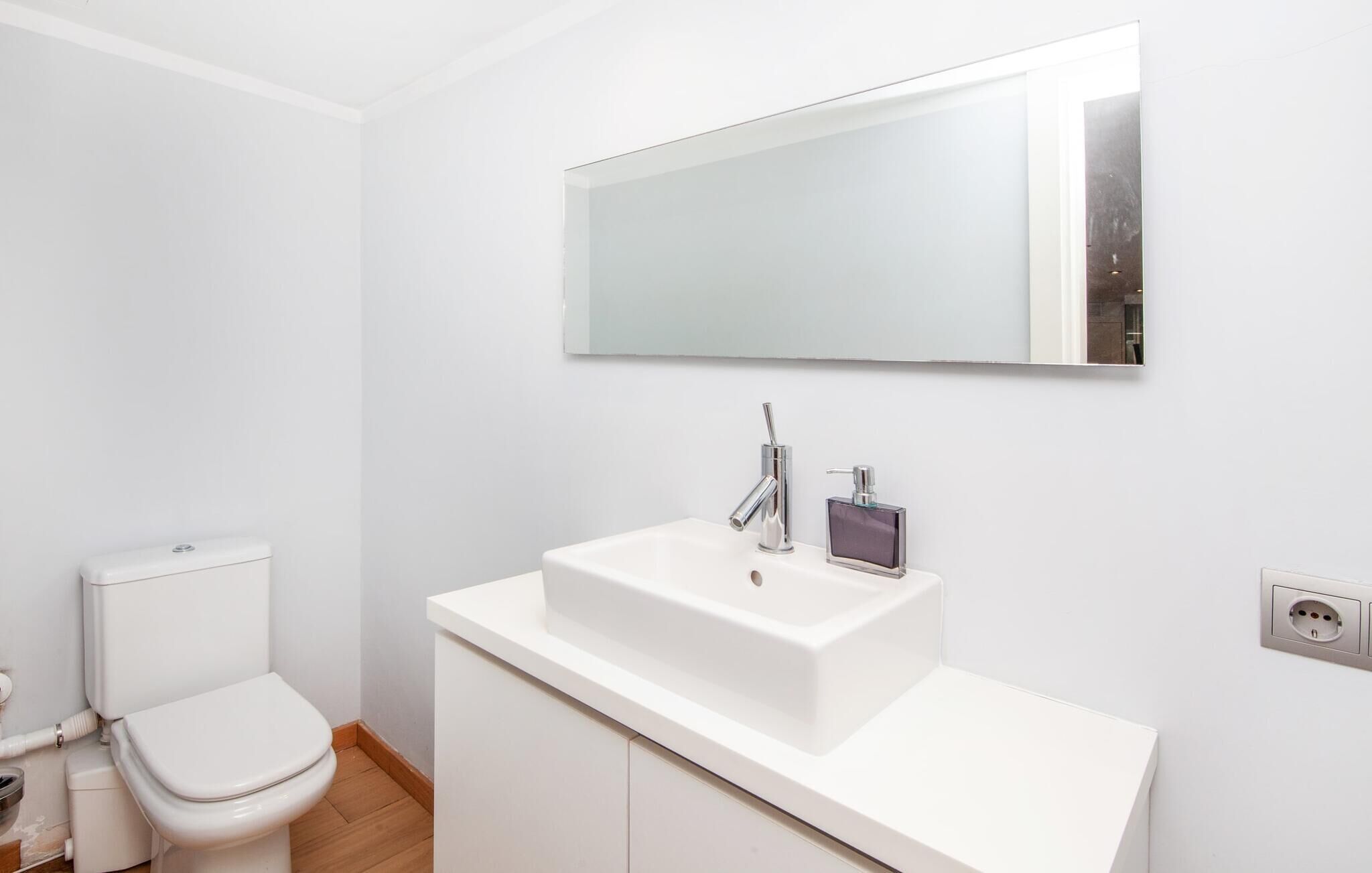 A modern bathroom with a white sink, a mirror, and a toilet.