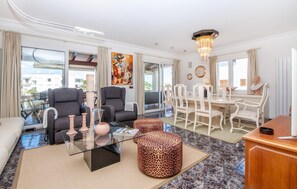 A modern living room with a glass coffee table, two grey armchairs, a white dining table with chairs, and a chandelier. - Awesome home in Portocolom with private swimming pool, can be inside or outside (Portocolom)