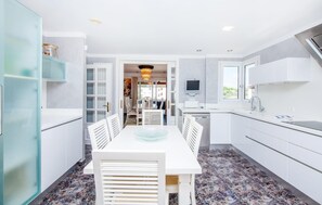 A modern kitchen with white cabinetry, a dining area with a glass table, and a view to the outside. - Awesome home in Portocolom with private swimming pool, can be inside or outside (Portocolom)