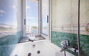 A bathroom with a bathtub, a window with blinds, and a view of buildings and water. - Awesome home in Portocolom with private swimming pool, can be inside or outside (Portocolom)