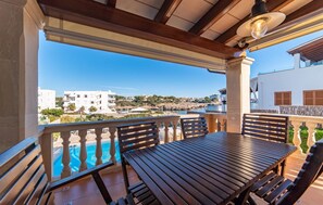 A wooden table and benches on a balcony with a view of a swimming pool and buildings in the background. - Awesome home in Portocolom with private swimming pool, can be inside or outside (Portocolom)