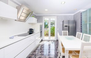 A modern kitchen with white cabinetry, a black countertop, and a built-in oven. There is a dining area with a white table and chairs, and a large window with a view of greenery. - Awesome home in Portocolom with private swimming pool, can be inside or outside (Portocolom)