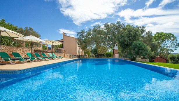 A swimming pool with lounge chairs and umbrellas, surrounded by trees and a stone wall. - Beautiful home in Felanitx with sauna (Felanitx)