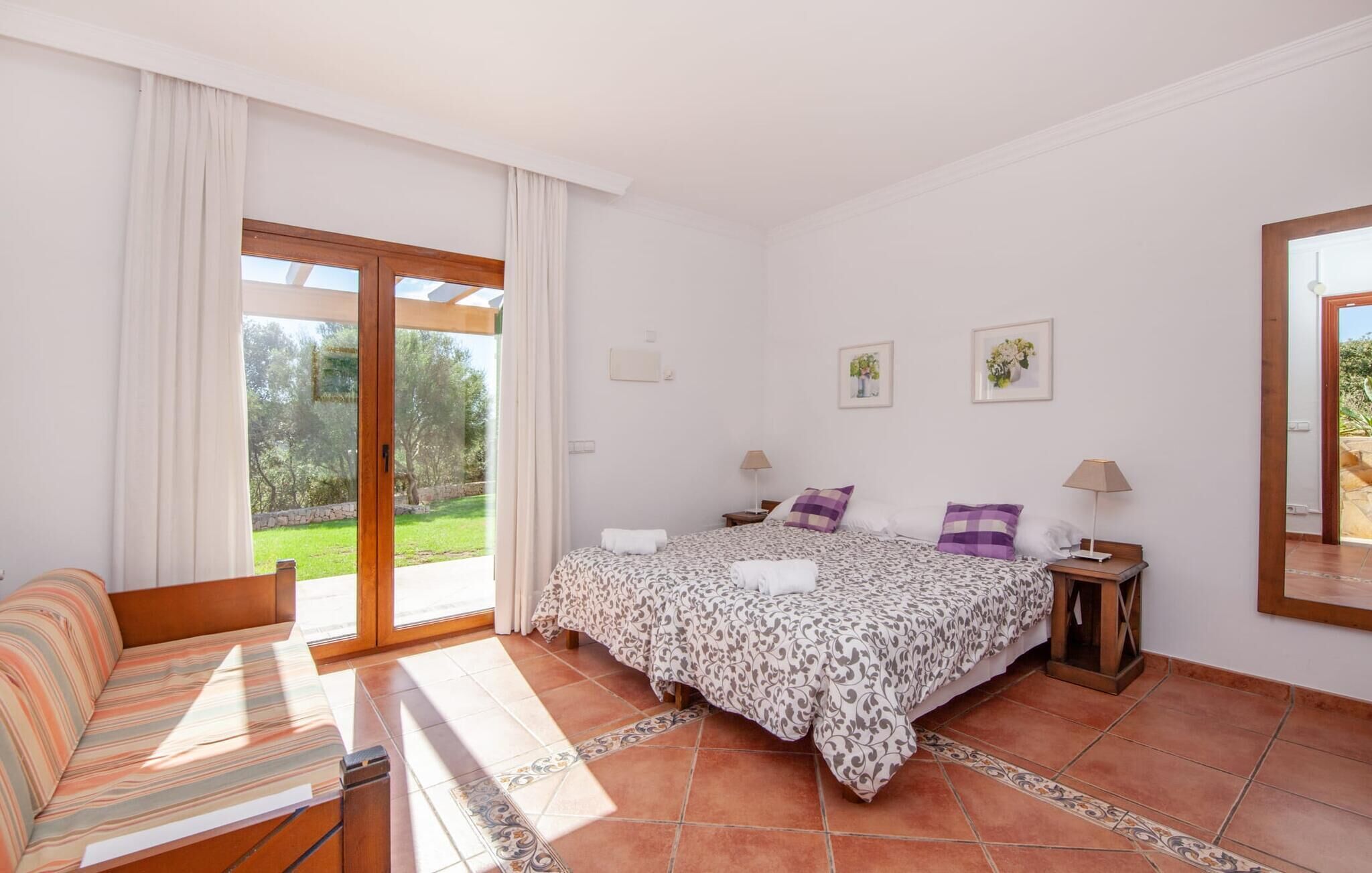 Un dormitorio con cama, sofá, mesita de noche y ventana con cortinas.