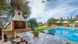 An outdoor pool area with a barbecue grill, wicker chairs, and a table with a potted plant. - Beautiful home in Felanitx with sauna (Felanitx)