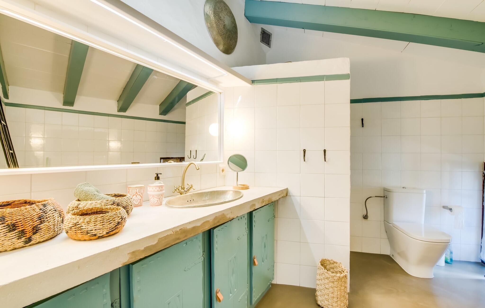 A bathroom with a sink, mirror, and toilet. There are wicker baskets on the counter.