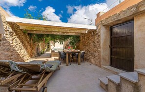 Ein Innenhof mit Steinmauern, einem Holztisch und -stühlen, einem kleinen Pool und einer Pergola mit Kletterpflanzen.