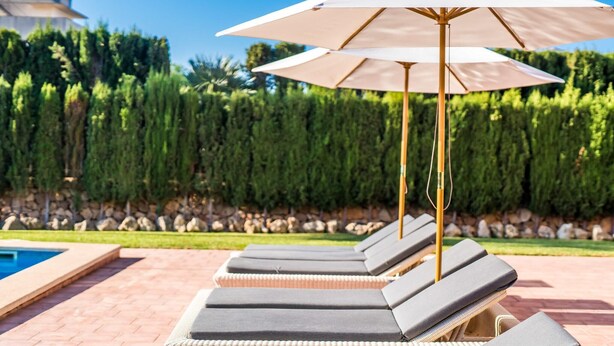 Een zwembadterras met ligbedden en een grote parasol.