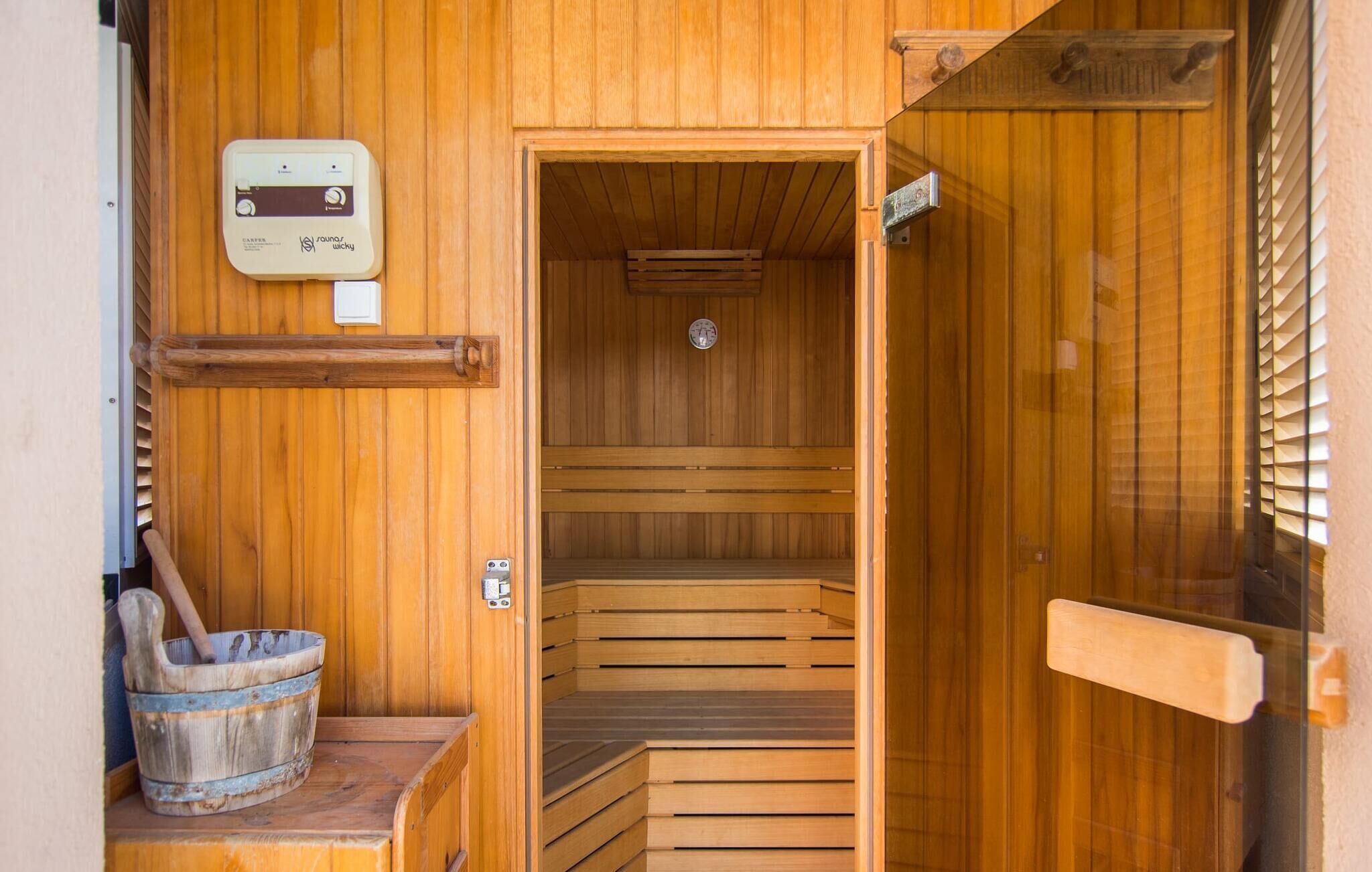 A wooden sauna with a control panel, a wooden bench, and a bucket.
